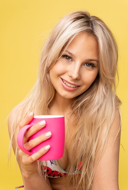 La bella ragazza beve il tè da una tazza rosa su sfondo giallo e sorride