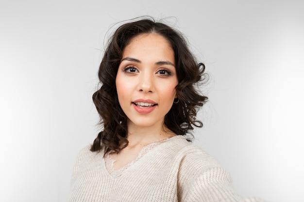 La bella ragazza castana con trucco fa il selfie su uno studio grigio