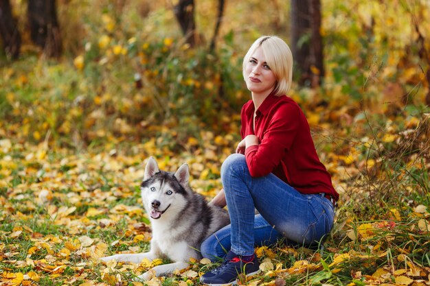 La bella ragazza caucasica gioca con il cane husky nella foresta o nel parco di autunno