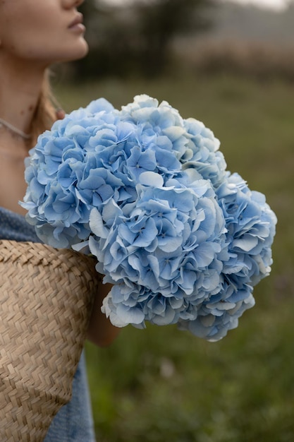 La bella ragazza caucasica in un vestito blu cammina attraverso il campo con un cesto di fiori