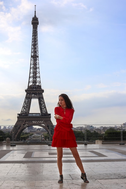 La bella ragazza con capelli marroni lunghi in vestito rosso resta davanti alla torre Eiffel