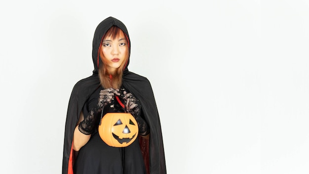 La bella ragazza con i capelli neri e arancioni in vestito nero e cappello della strega sta tenendo il concetto di Halloween della zucca