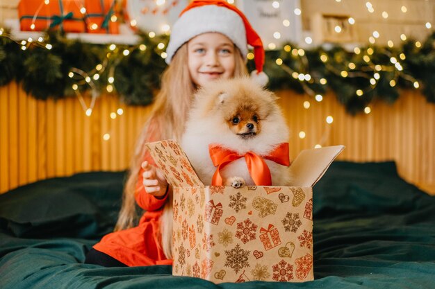 La bella ragazza con il cappello di Babbo Natale ha ricevuto un cucciolo come regalo per il nuovo anno, la magia e il miracolo del Natale, i sogni diventano realtà