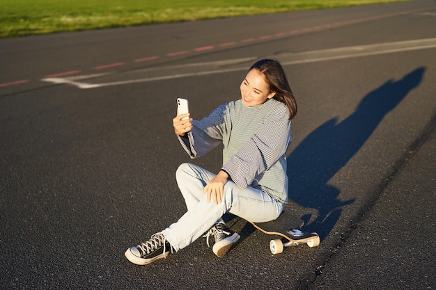 La bella ragazza coreana scatta selfie sullo smartphone scatta foto con il suo skateboard enoys giornata di sole fuori