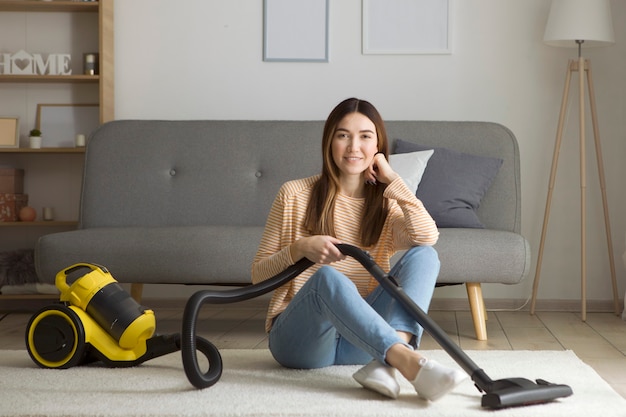 La bella ragazza di buon umore fa le pulizie di casa con un aspirapolvere