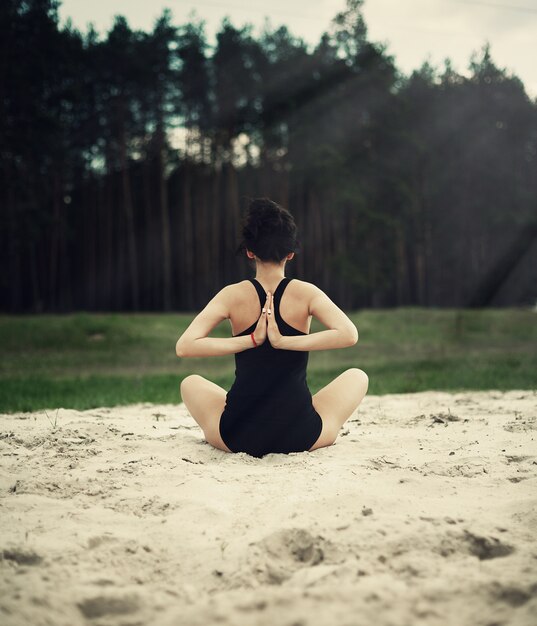 La bella ragazza è impegnata nello yoga nella foresta sulla sabbia