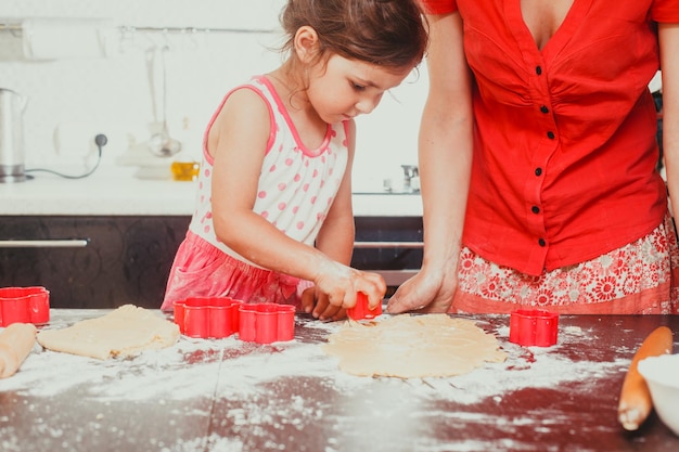 La bella ragazza fa delle forme di pasta a forma di fiore, e la mamma accanto a lei in cucina