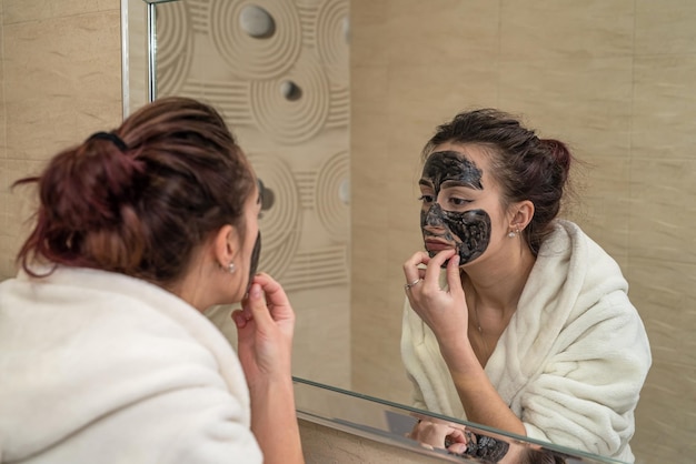 La bella ragazza fa una maschera nera per l'acne sul viso