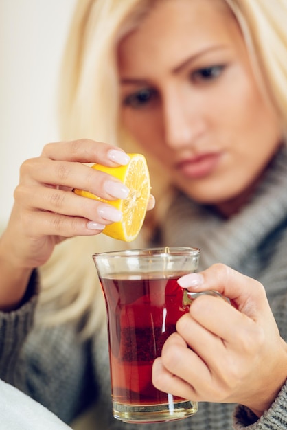 La bella ragazza ha spremuto il limone in una tazza di tè. Messa a fuoco selettiva. Concentrati sul primo piano, sulla tazza di tè e sul limone.