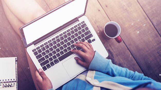 La bella ragazza ha usato la tazza di caffè e del computer portatile in mani della ragazza che si siedono su un pavimento di legno