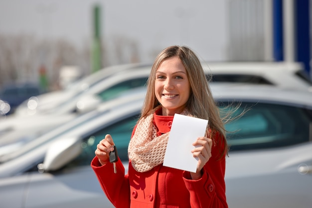 La bella ragazza in cappotto rosso tiene le chiavi di una nuova automobile. Acquisto di un'auto