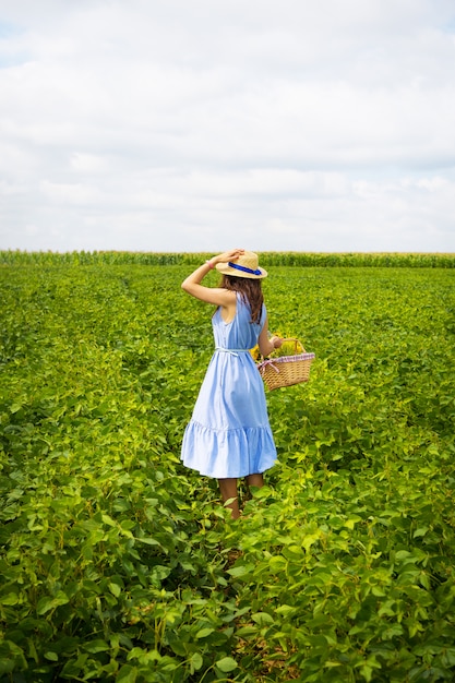 La bella ragazza in un cappello e un bordo blu sta stando su un campo verde