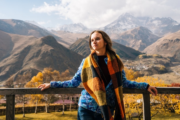 La bella ragazza in una giacca calda viaggia, sta in mezzo ad alte montagne e gode della natura