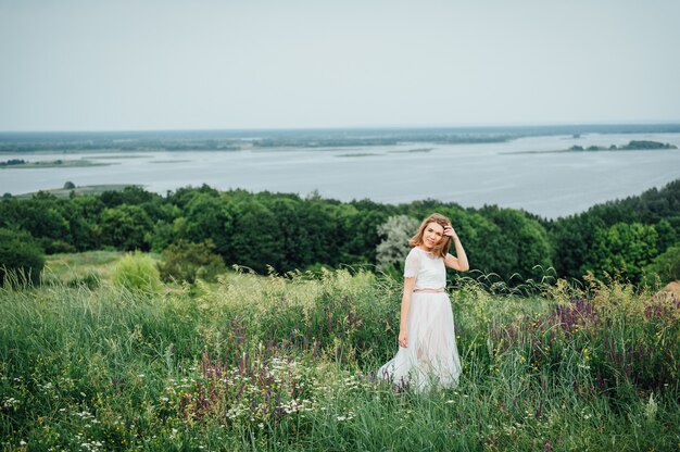 La bella ragazza in vestito bianco si trova in erba verde