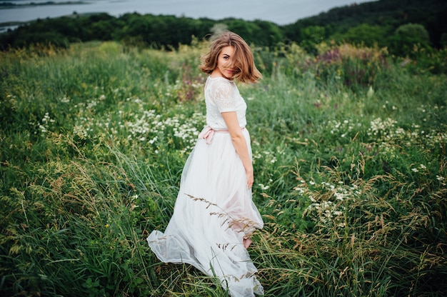 La bella ragazza in vestito bianco si trova in erba verde