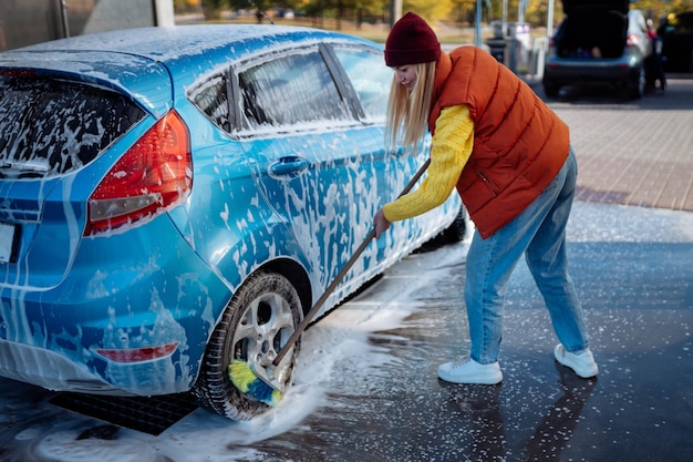 La bella ragazza lava l'auto all'autolavaggio self-service. cancellare lo sporco dall'auto con un pennello