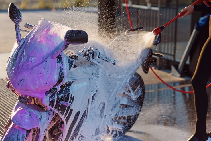 La bella ragazza lava una motocicletta all'autolavaggio self-service con acqua ad alta pressione