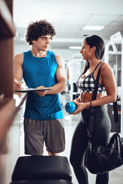 La bella ragazza muscolare si consulta con l'istruttore prima dell'allenamento in palestra.