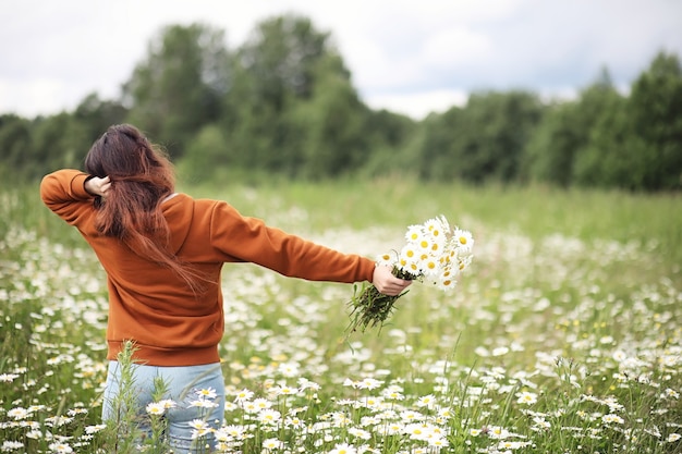 La bella ragazza raccoglie le margherite nel giorno di estate in afield