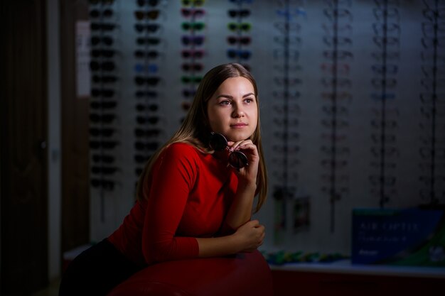 La bella ragazza sceglie gli occhiali da sole in un negozio di ottica.