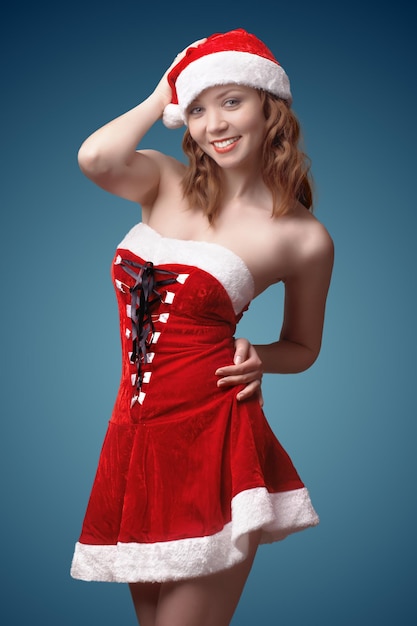 La bella ragazza sexy vestita come aiutante di Babbo Natale sta posando. su sfondo blu
