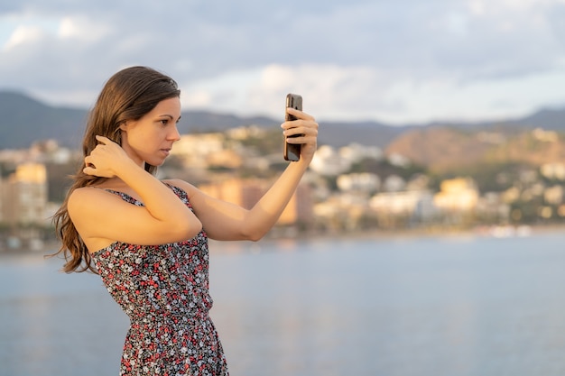 La bella ragazza si aggiusta i capelli usando la fotocamera del suo telefono