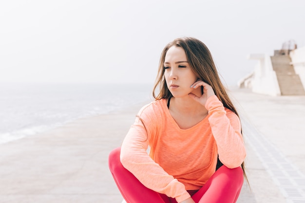 La bella ragazza si siede sulla spiaggia al mattino e guarda il mare