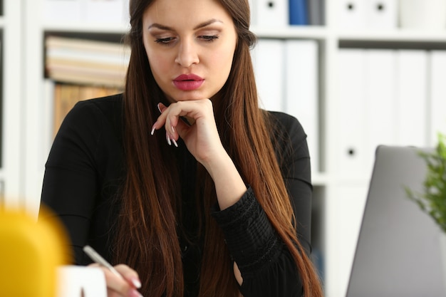 La bella ragazza sorridente al posto di lavoro tiene la penna d'argento