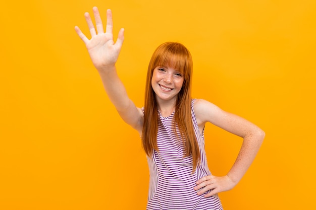 La bella ragazza sorridente dai capelli rossi in una maglietta fa smorfie che esaminano la macchina fotografica sopra variopinto giallo