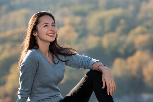 La bella ragazza sorridente si siede su una parete di una foresta. Giorno soleggiato