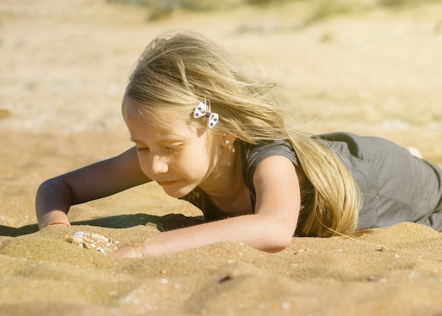 La bella ragazza sotto i raggi del sole guardava da vicino la sabbia del mare.