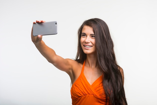 La bella ragazza sta tenendo la macchina fotografica e sta facendo la foto. La giovane signora si diverte su sfondo bianco.