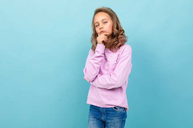 La bella scolara in camicetta viola pensa allo studio isolato sull'azzurro