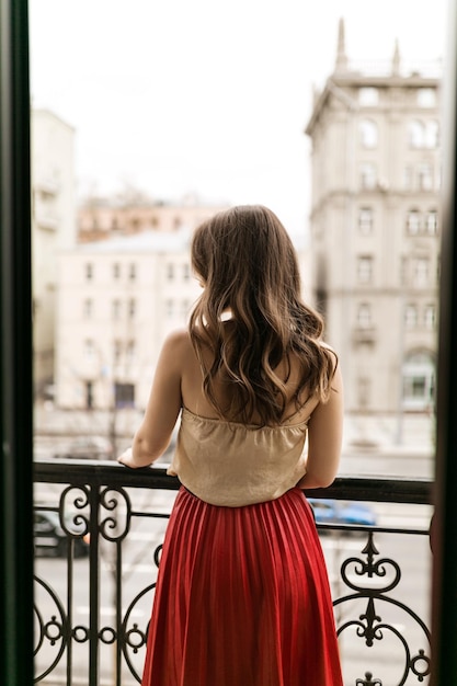 La bella signora sta sul balcone, lunghi capelli ricci e gonna rossa. La signora sta guardando la strada della città