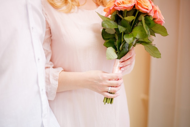 La bella sposa con un anello al dito tiene in mano un mazzo di rose rosa.