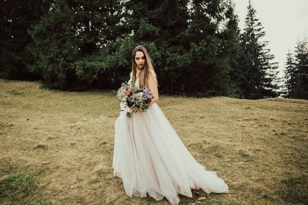 La bella sposa tiene e guarda un bouquet da sposa