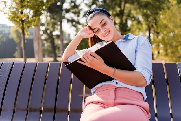 La bella tenuta della giovane donna apre il libro e lettura sul banco nel parco di autunno