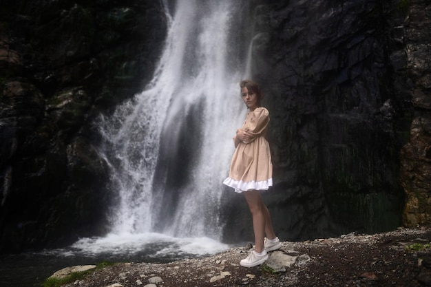 La bellissima modella con un vestito beige posa vicino alla cascata