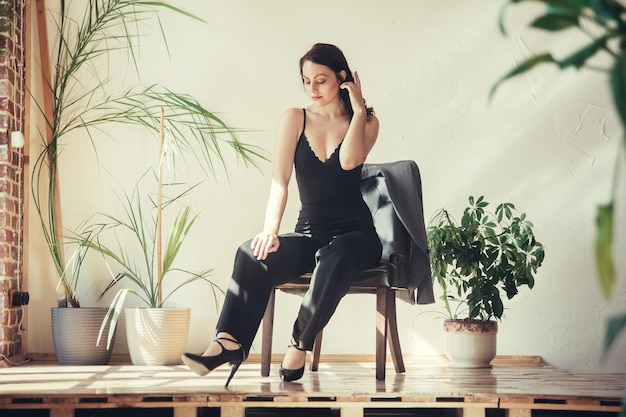 La bellissima modella vestita di nero si siede su una sedia in interni in stile loft