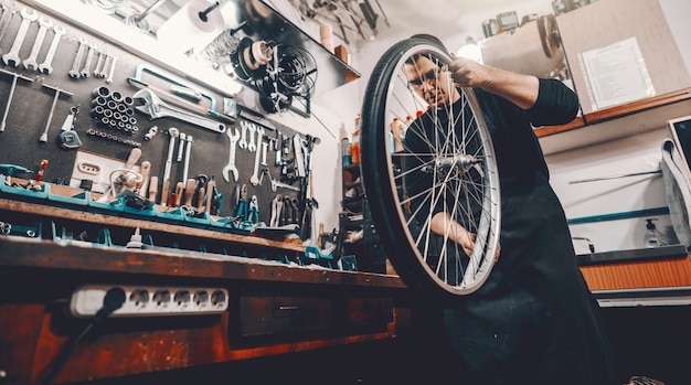 La bicicletta caucasica bella seria della tenuta dell'uomo spinge dentro le mani mentre sta nell'officina.