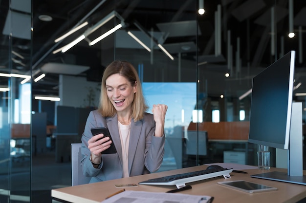 La bionda felice si rallegra della donna d'affari che lavora in ufficio con un telefono felice incontro online incontri