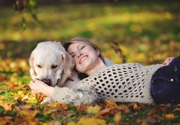 La bionda giace in foglie gialle con il suo labrador nel parco in autunno