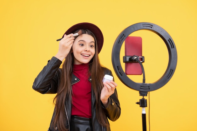 La blogger felice della ragazza adolescente usa la lampada a led selfie e lo smartphone sul treppiede per realizzare tutorial video online blog di bellezza che presentano blog di pennelli per cipria