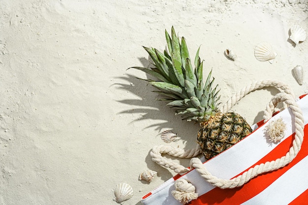 La borsa da spiaggia con ananas si trova sulla sabbia bianca sulla spiaggia
