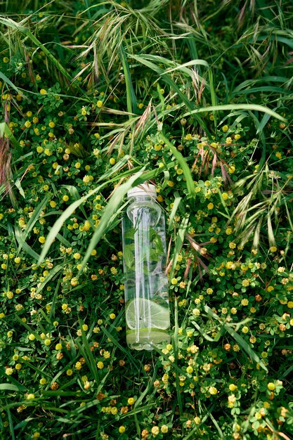 La bottiglia d'acqua giace sull'erba alta verde tra i fiori di campo