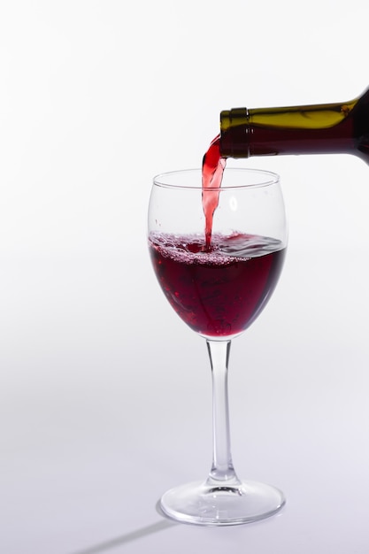 La bottiglia di vino rosso versa il vetro su fondo bianco