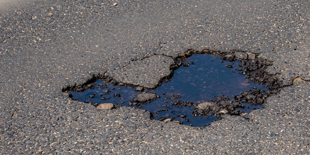 La buca sulla strada contiene una pozza d'acqua a specchio che riflette il cielo