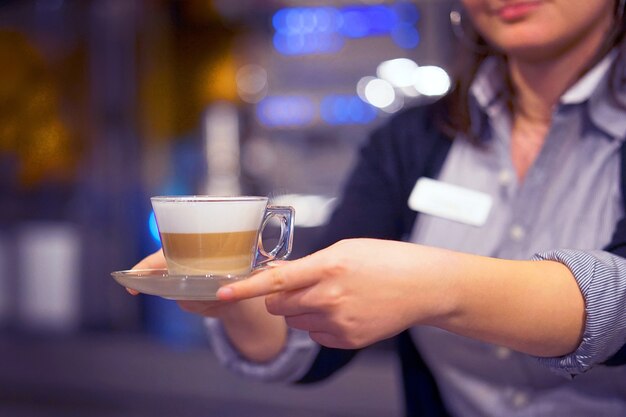 La cameriera dà una tazza di caffè-cappuccino a un cliente in un ristorante. Il concetto di servizio e manutenzione.