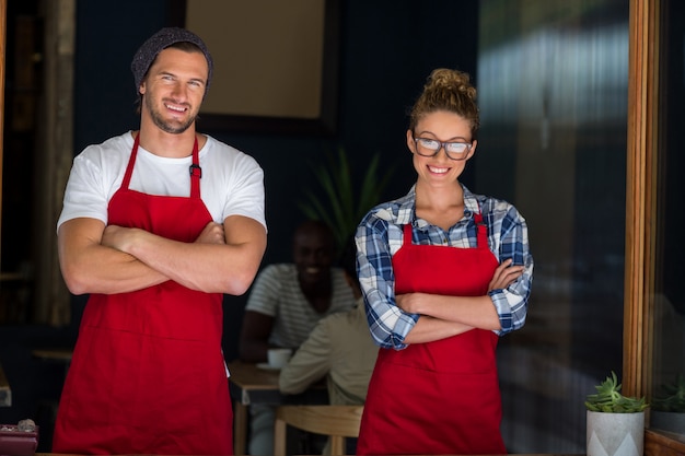 La cameriera di bar e il cameriere sorridenti che stanno con le armi hanno attraversato il caffè esterno