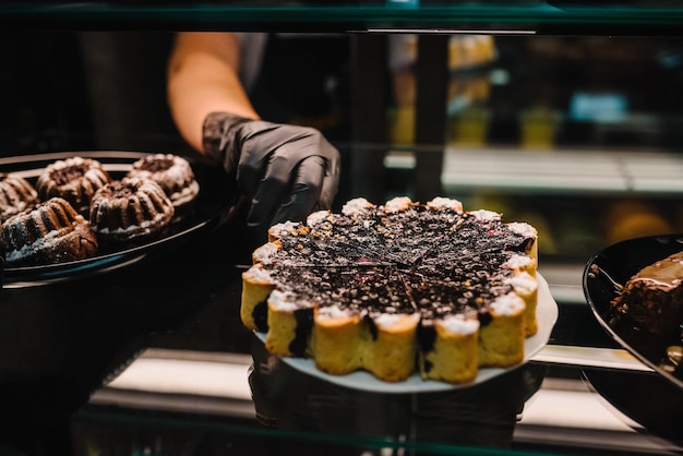 La cameriera prende la torta su un display di vetro al bar Mani femminili che offrono pasticceria fresca in un negozio di dolciumi